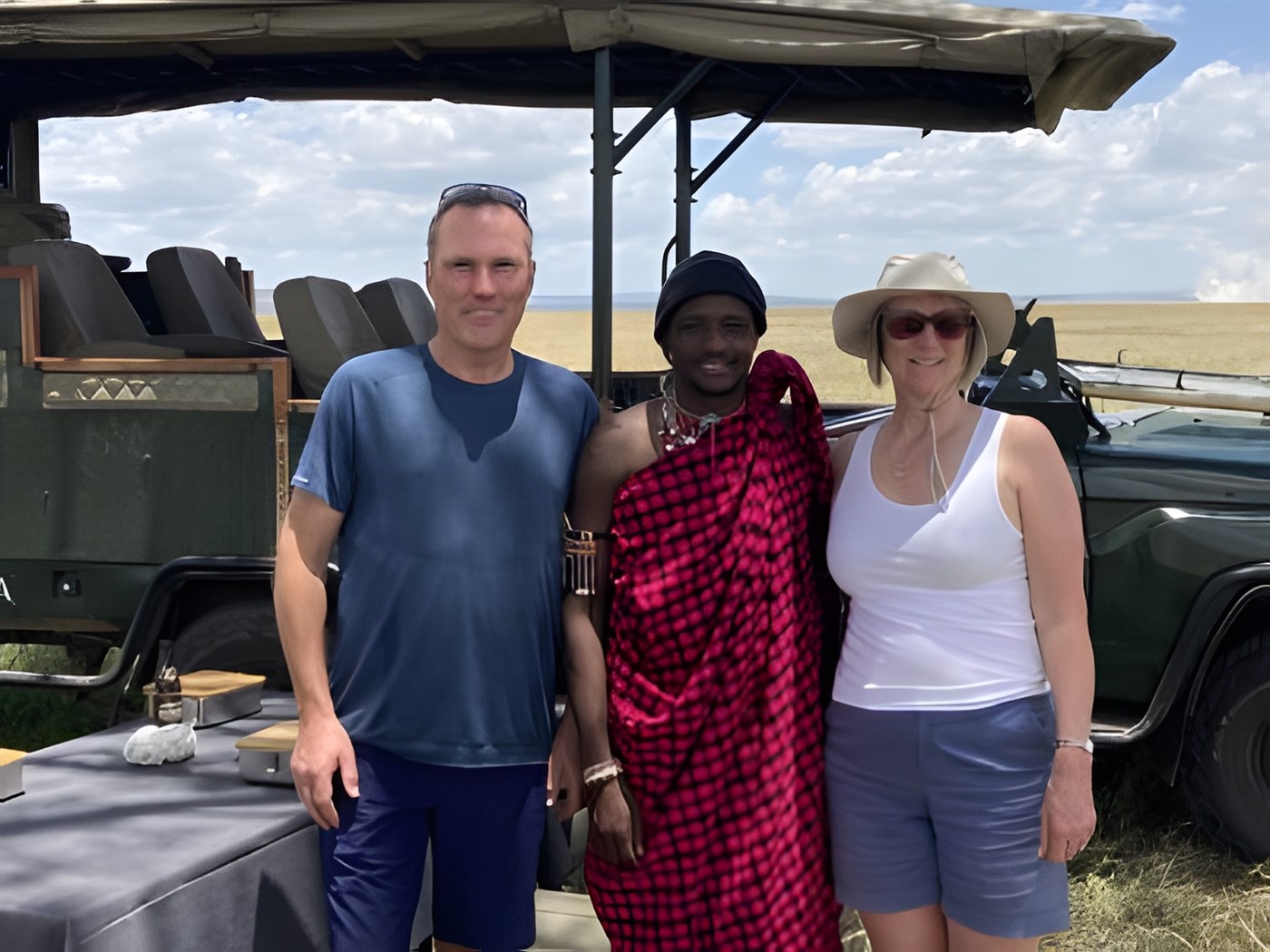 A couple stand with a Masai safari guide in front of a safari vehicle