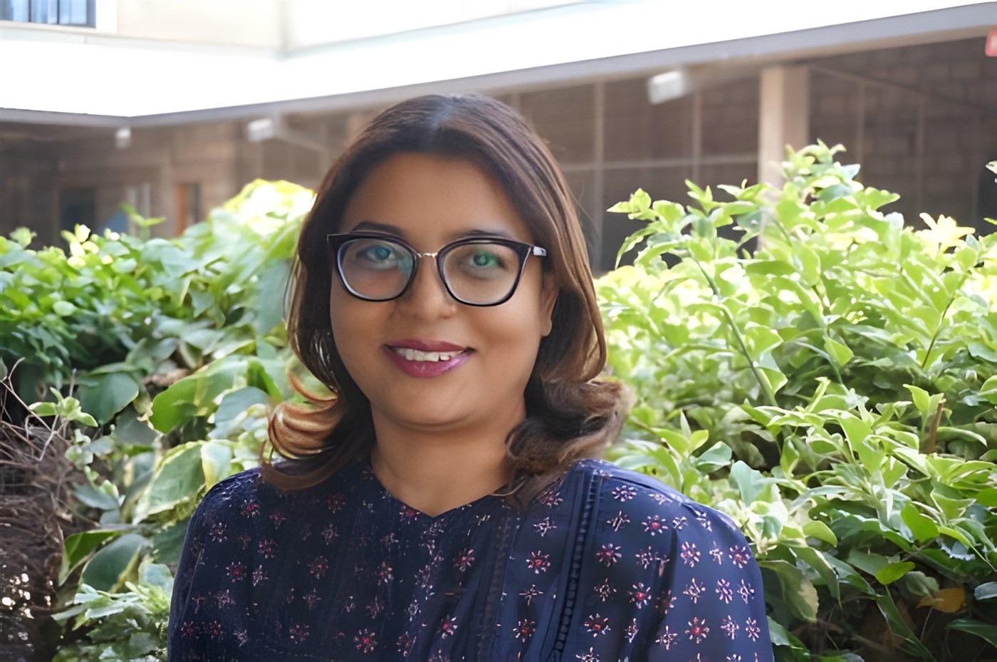 Lady wearing navy blue blouse and glasses standing in front of greenery