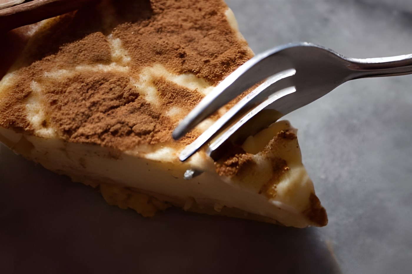 A slice of Melktert with a cake fork cutting pushing into it as if a diner out of frame is about to eat a mouthful. The melktert (milk tart) is a traditional South African dessert.