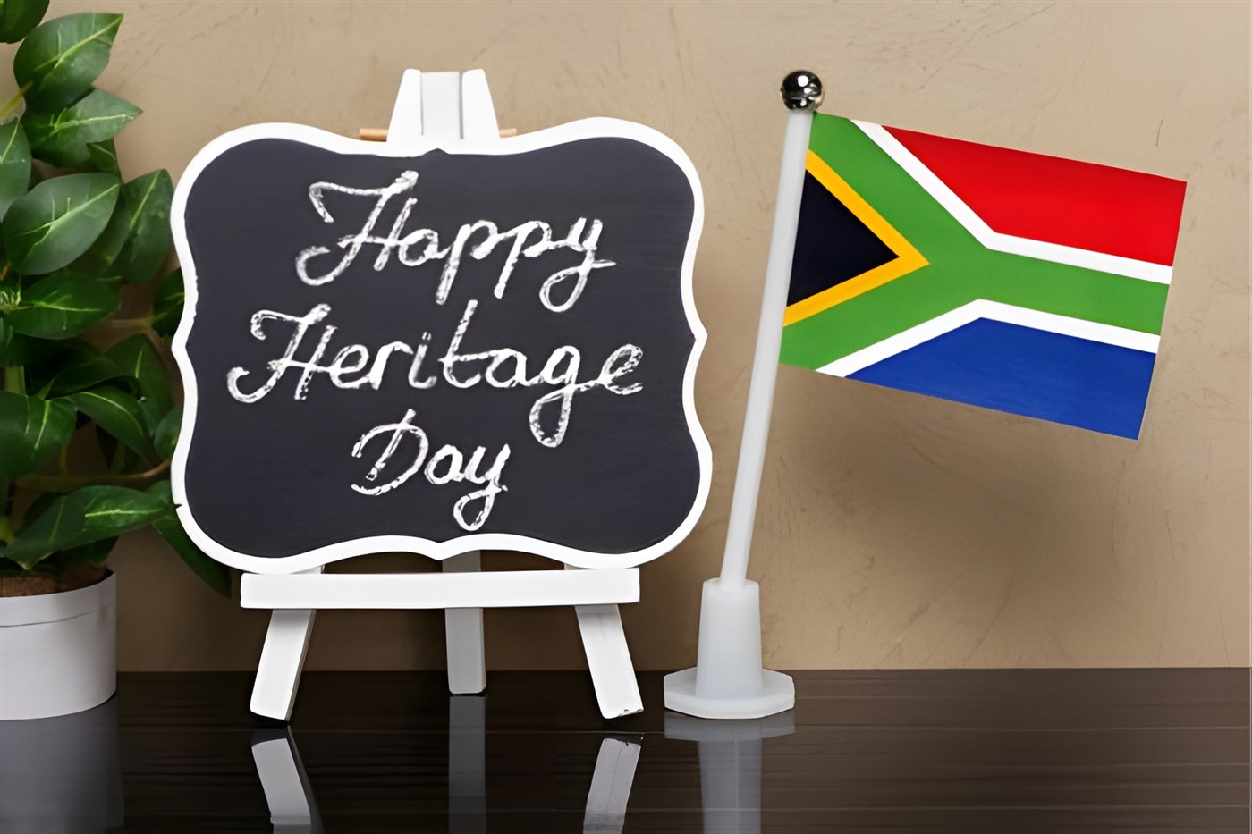 Small sign on small easel painted white next to small south african flag. the sign reads Happy Heritage Day
