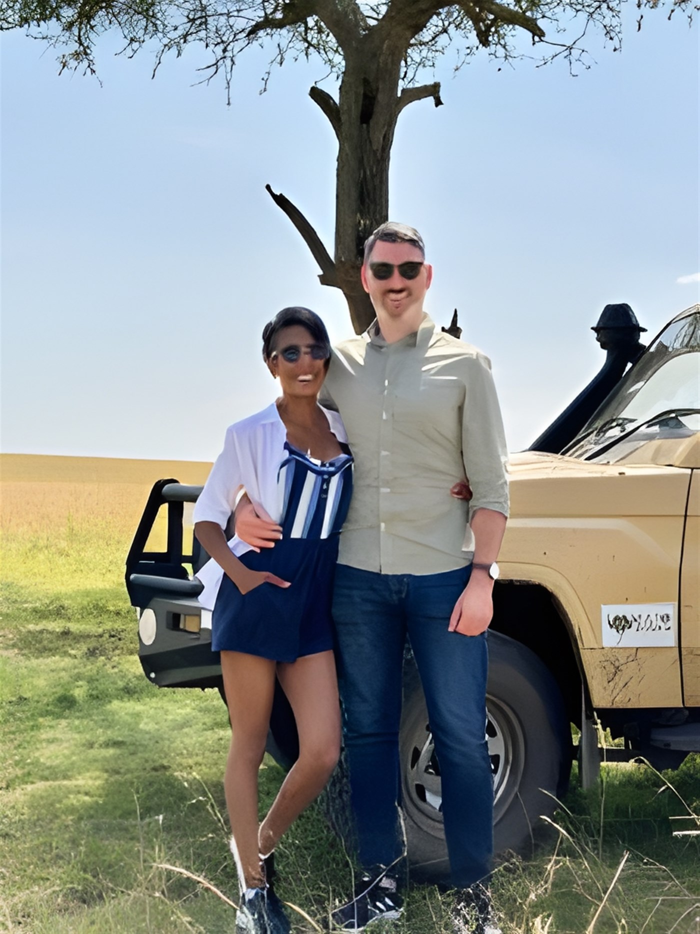 Sheree and Sean stand in the shade of a tree, in front of the Safari 4x4 vehicle, both wearing sunglasses.