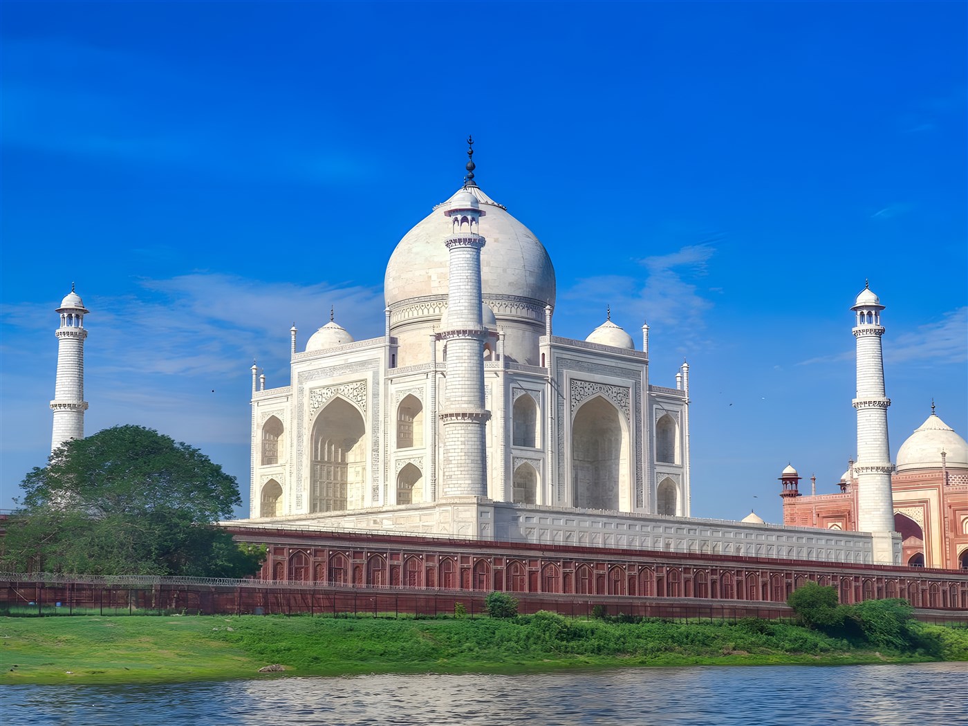 Tah Mahal with a brilliant Blue Sky and green grass and river in the foreground. 