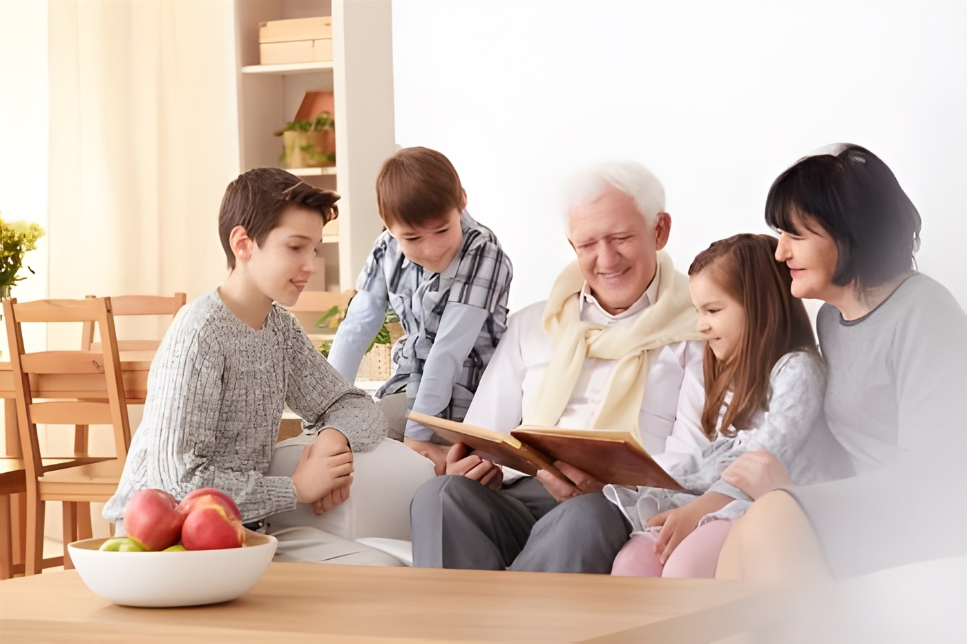 A family group spanning three generations with grandparents and children looking through a photo album to illustrate that family vacations are a great way to make long lasting memories