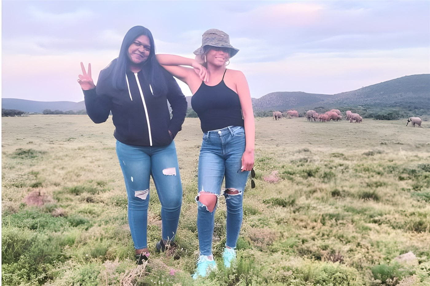 Celeste and Sam on safari in the Eastern Cape, South Africa. Standing in a field with a herd of elephants in the far distance.