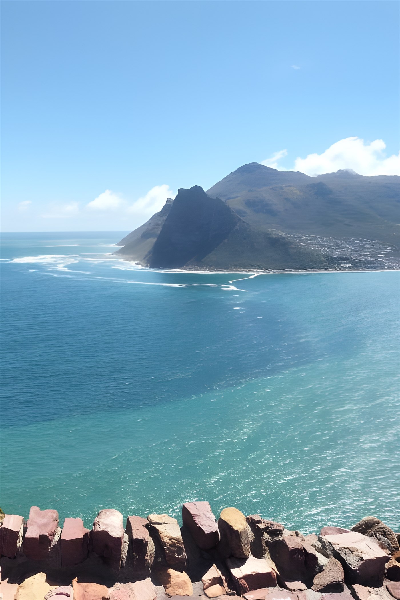 Rock wall in the foreground with the sea and mountains in the middle distance and background. The view from Chapman's Peak Drive, Cape Town, South Africa