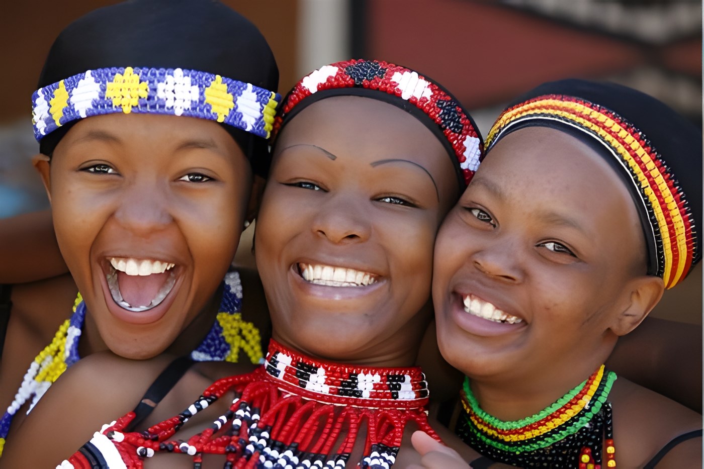 Three young women wearing traditional zulu beadwork headbands and necklaces smiling at the camera, the one of the far left has her mouth open in a laugh. Stock Image from Canva Pro.