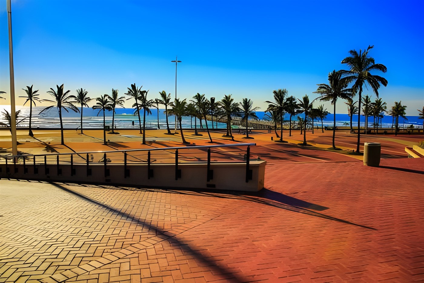 A vibrant view of the North Beach promenade in Durban, South Africa, with palm trees lining the golden sands and the sparkling ocean under a clear blue sky.