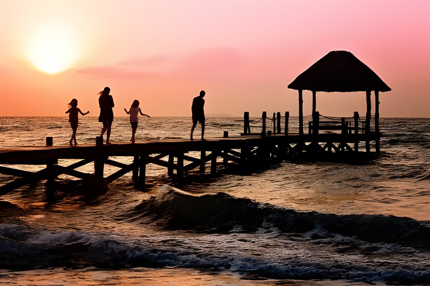 Family frolicing on a jetty over the sea water lapping on a beach in a blog about family travel which includes beach destinatinons