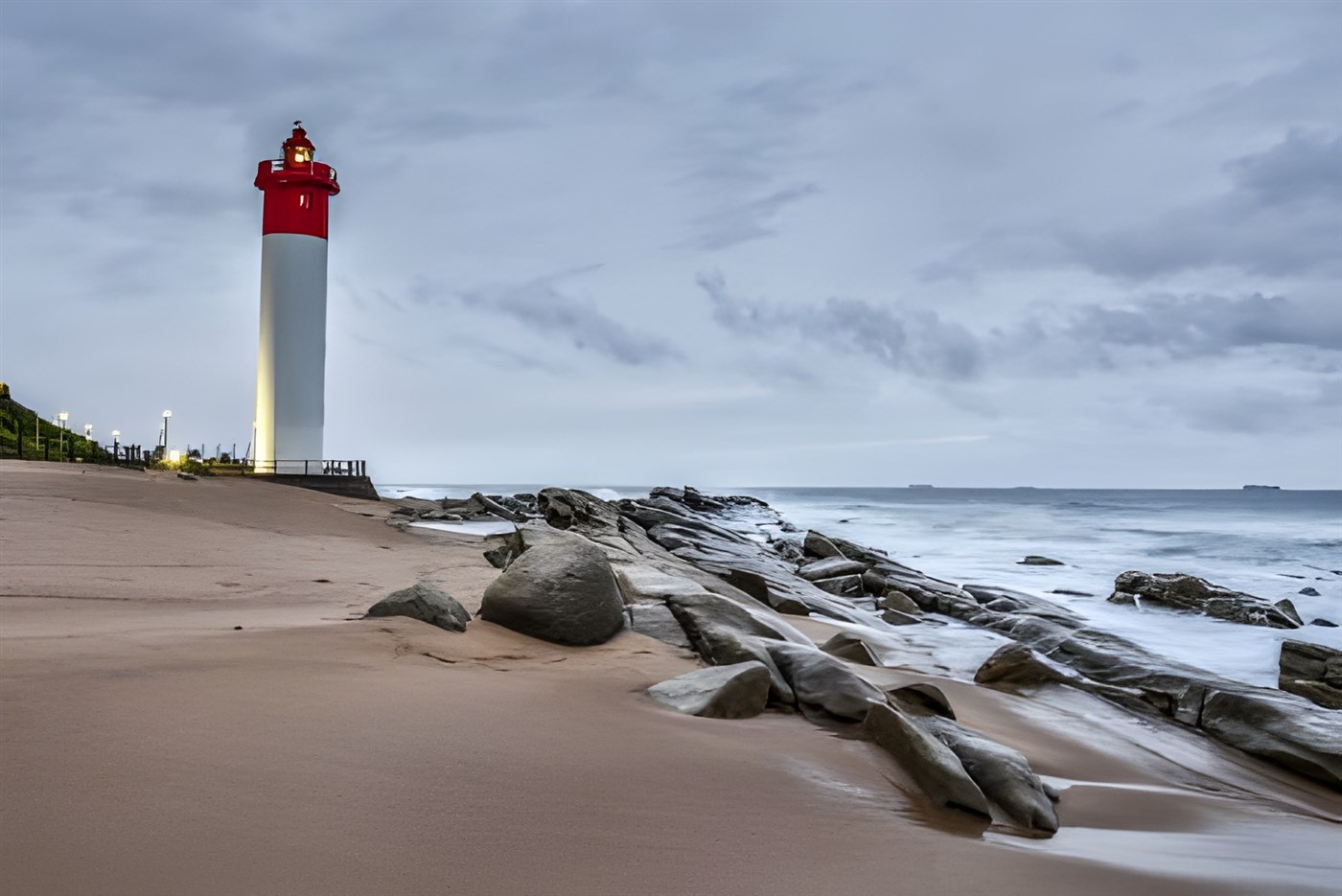 The iconic red and white lighthouse at uMhlanga Rocks, KwaZulu-Natal, South Africa, standing on the beautiful sandy beach with scattered rocks.