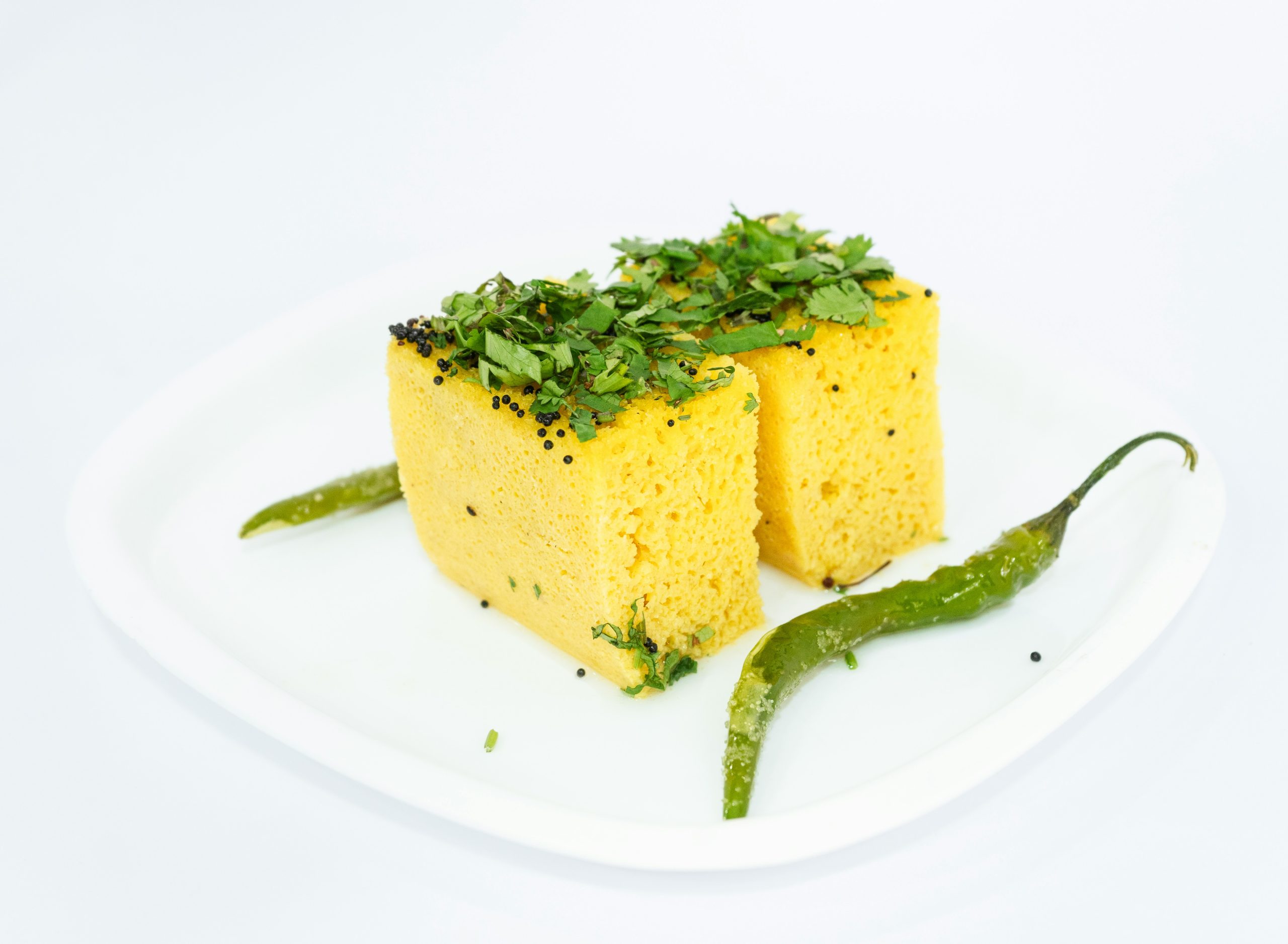 Two pieces of fluffy yellow Dhokla covered in green with spices