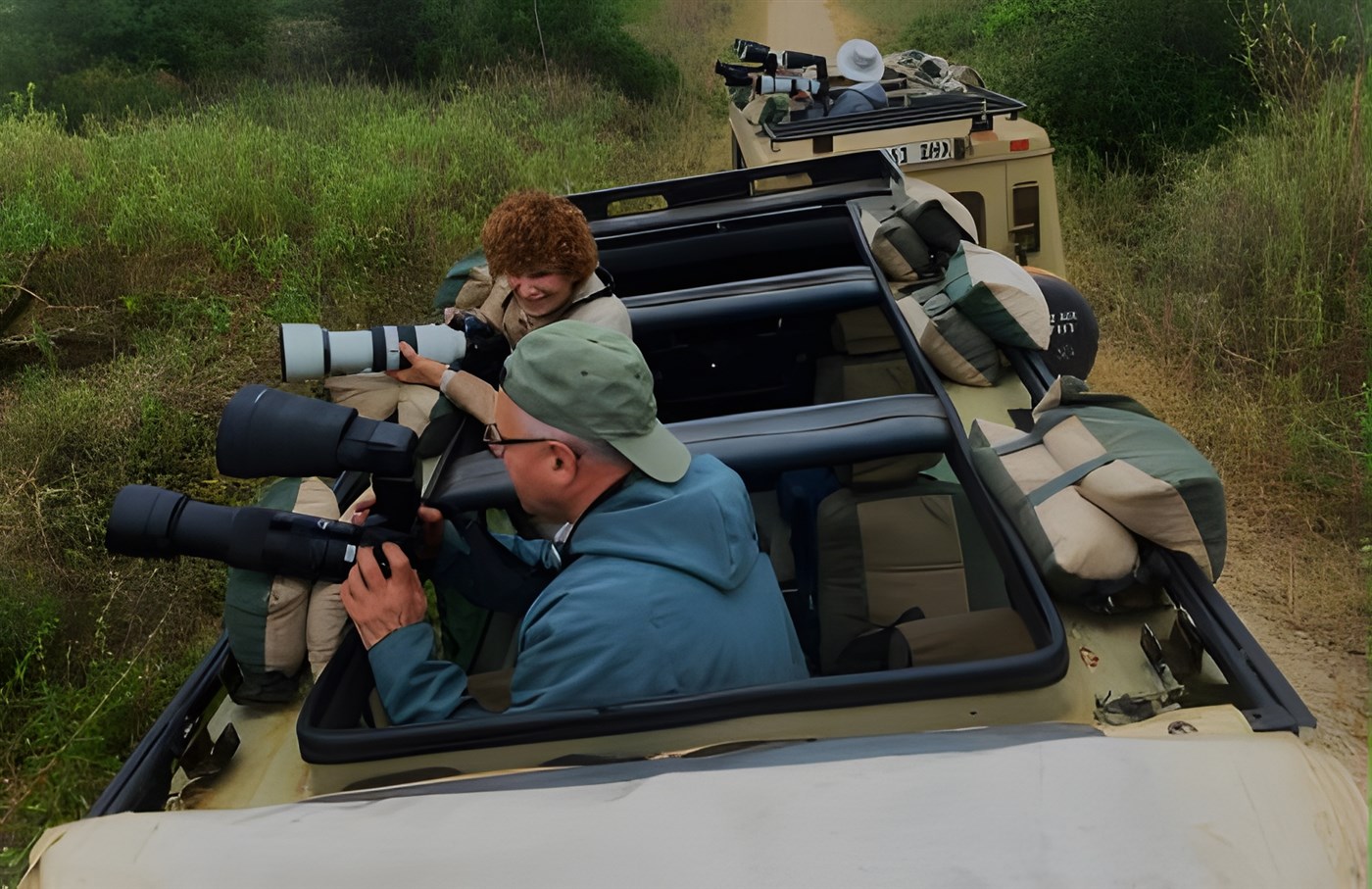 Photographers with professional gear and lenses in a safari vehicle.