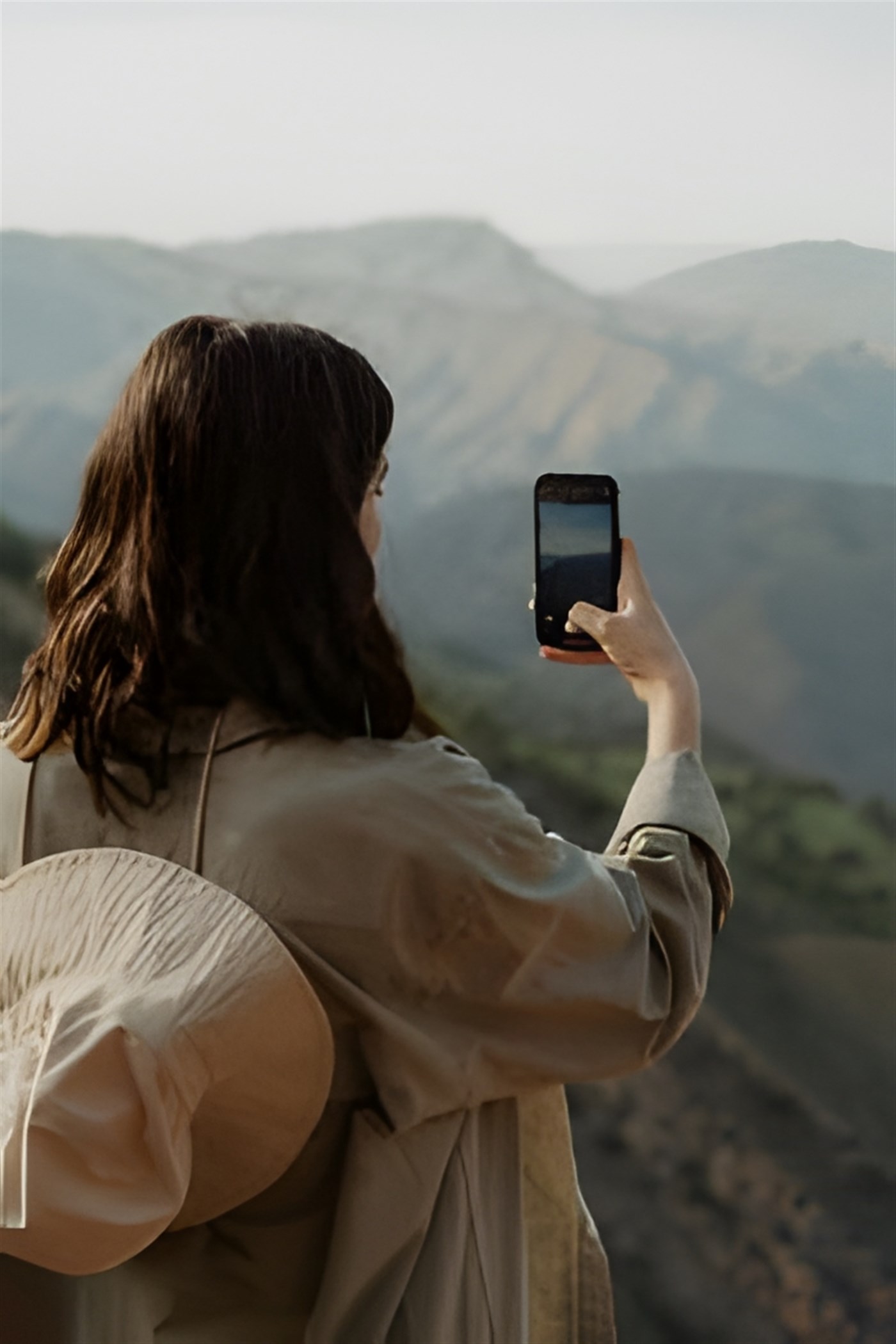 Photo of a woman using a smartphone to take a photograph of landscapes.